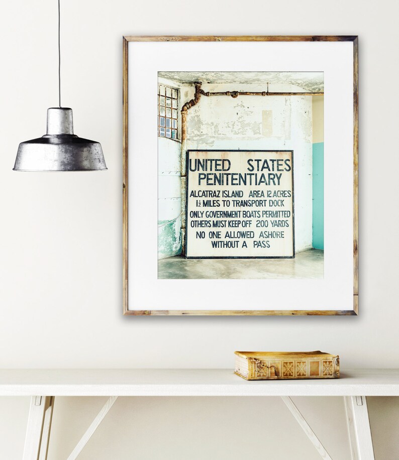 May include: A black and white photograph of a sign that reads "United States Penitentiary" with the text "Alcatraz Island Area 12 Acres 1 1/2 Miles to Transport Dock Only Government Boats Permitted Others Must Keep Off 200 Yards No One Allowed Ashore Without A Pass".