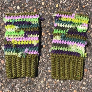 May include: A pair of handmade crochet fingerless gloves. The gloves feature a ribbed olive green cuff and a colorful pattern of green, purple, and lavender. The gloves are designed to keep hands warm while leaving fingers free.