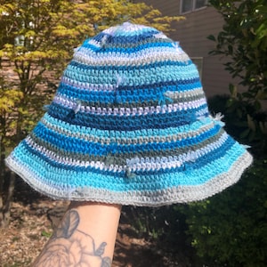 May include: A blue, white, and gray striped crocheted bucket hat with a textured surface.