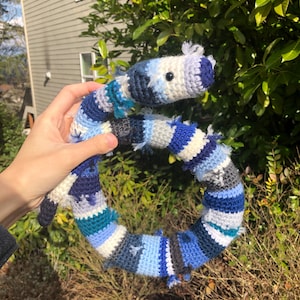 May include: A crocheted snake toy made with blue, white and black yarn. The snake is curled into a circle and has black eyes.