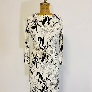 May include: A white dress with a black floral print and a tie at the waist.