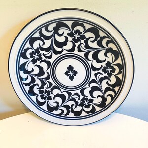 Op de afbeelding: Een ronde, witte serveerschaal met een marineblauw bloemmotief. De schaal heeft een marineblauwe rand en een centraal bloemmotief. Het ontwerp toont gestileerde bloemen en wervelende patronen.