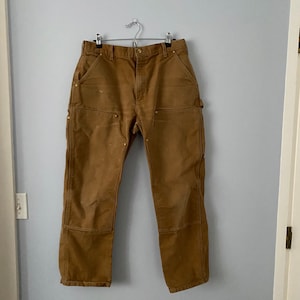 Può includere: Un paio di pantaloni da lavoro marroni con più tasche e un passante per martello.