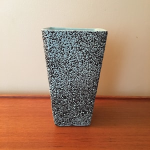 May include: A light blue ceramic vase with a textured black glaze. The vase has a square shape and a wide opening.