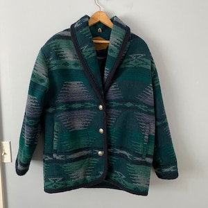 Puede incluir: Una chaqueta de patrón verde y azul con cuello chal y cierre de botón. La chaqueta tiene un diseño del suroeste.