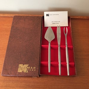 Puede incluir: Un juego de tres utensilios para aperitivos plateados en una caja forrada de terciopelo rojo. La caja es marrón con las palabras "Kalmar Designs" impresas en la parte delantera. La tarjeta dentro de la caja dice "3 PC. SNACK SET FROM ITALY."