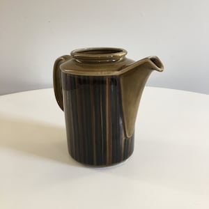 Puede incluir: Una tetera de cerámica marrón con un diseño a rayas. La tetera tiene un asa y un pico.