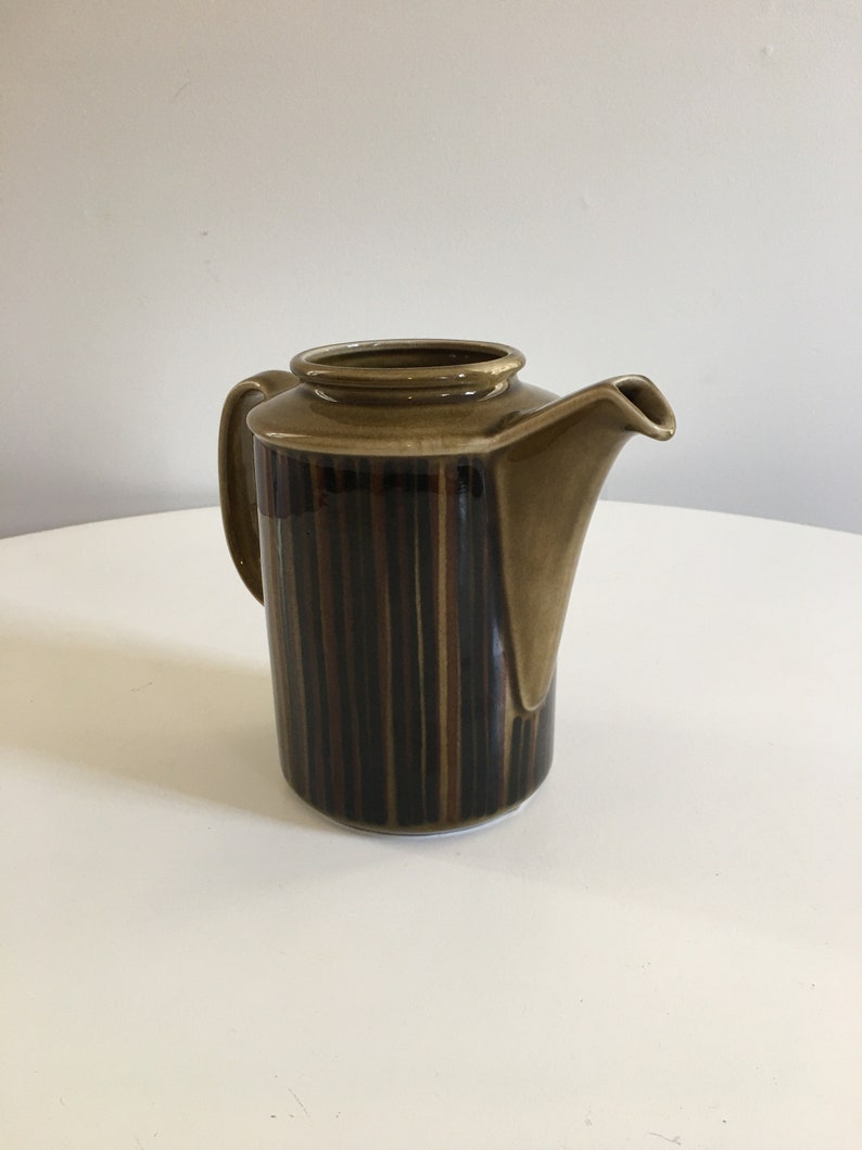 Puede incluir: Una tetera de cer&aacute;mica marr&oacute;n con un dise&ntilde;o a rayas. La tetera tiene un asa y un pico.