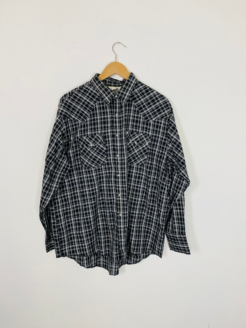May include: A black and white plaid long-sleeve button-down shirt with two chest pockets and a pointed collar.