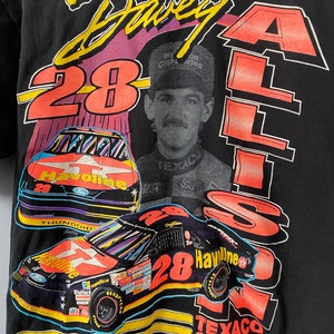 May include: A black t-shirt featuring a colourful graphic of race car driver Davey Allison. The graphic includes his car number 28, the Texaco Havoline logo, and his name in a stylised font.