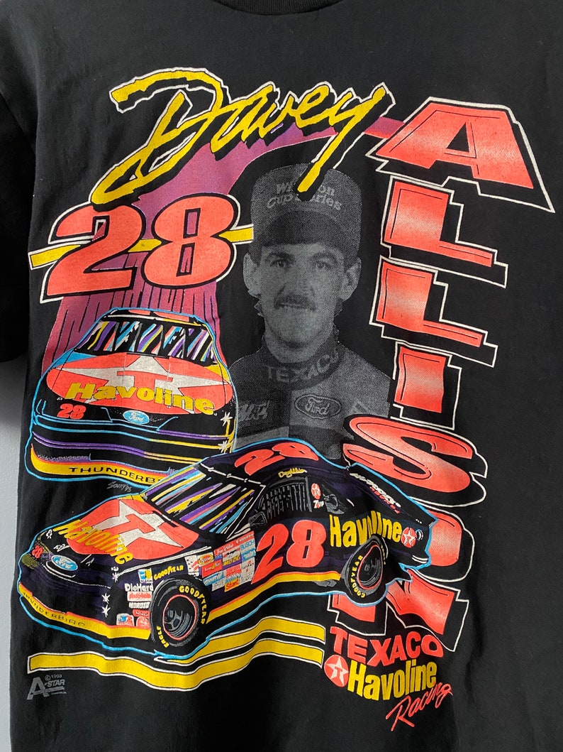 May include: A black t-shirt featuring a colourful graphic of race car driver Davey Allison. The graphic includes his car number 28, the Texaco Havoline logo, and his name in a stylised font.
