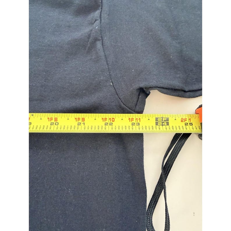 Może przedstawiać: Czarny t-shirt jest mierzony ż&oacute;łtą miarką. Miarka pokazuje pomiar około 61 cm. Koszulka jest wykonana z miękkiego materiału.