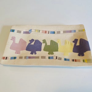Puede incluir: Una bandeja rectangular de servir de cerámica con fondo blanco y borde de colores. El borde presenta un patrón repetitivo de rayas en varios colores, incluyendo azul, verde, amarillo y rojo. Cinco pájaros estilizados se representan en una fila a través del centro de la bandeja, cada uno pintado en un color diferente: rosa, morado, verde, amarillo y morado.