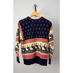 May include: A vintage navy blue sweater with a colorful peacock design. The sweater features a crew neck, long sleeves, and a ribbed hem. The design includes a cream-colored background with rows of peacocks, red and brown accents.
