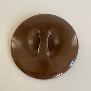 May include: A brown ceramic lid with a raised handle in the center. The lid is smooth and glossy.