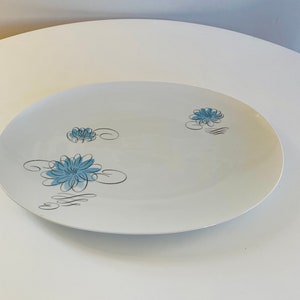 May include: A white oval serving platter with a blue and black floral design. The design features stylised blue flowers with black outlines and swirls.