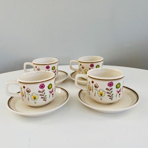 Puede incluir: Juego de cuatro tazas de té y platillos de cerámica vintage con un patrón floral en tonos rosa, verde y marrón. Las tazas y los platillos tienen un esmalte beige moteado.