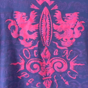 May include: A purple t-shirt with a pink graphic design of a stylized fleur-de-lis with two lions on either side. The graphic says "Ocean Pacific" in a stylized font.