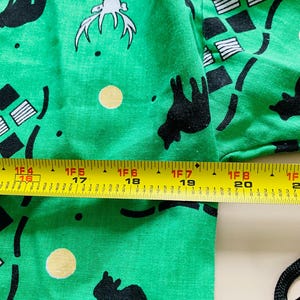 Puede incluir: Tela verde brillante con un patr&oacute;n repetido de siluetas de animales negros, formas geom&eacute;tricas y figuras blancas con cuernos. Una cinta m&eacute;trica amarilla muestra una longitud de aproximadamente 46 cm.