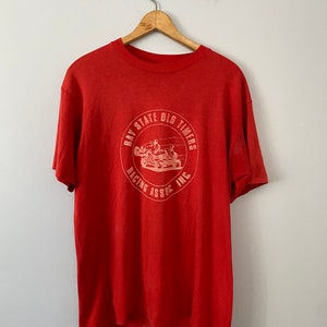 Op de afbeelding: Rood T-shirt met een witte afbeelding van een raceauto en de tekst "Bay State Old Timers Racing Assoc. Inc."