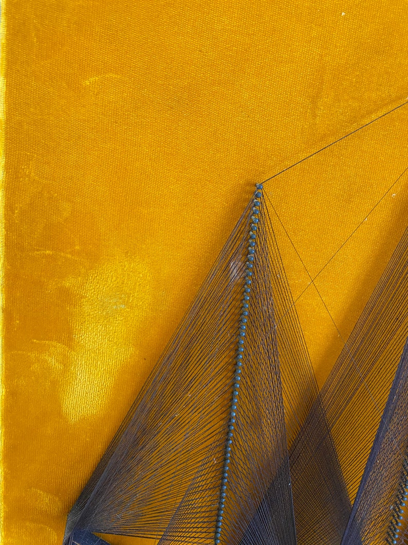 May include: A string art piece with a geometric design. The art is made with black thread and blue beads, and is mounted on a yellow velvet background.