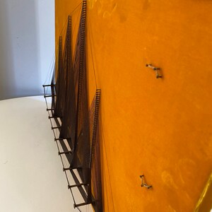 May include: A wall hanging made of string and wood, with a geometric design. The string is stretched taut between the wood pieces, creating a series of triangles. The background is a bright yellow.