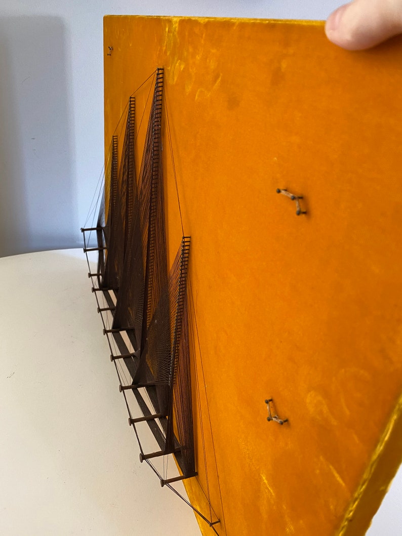 May include: A wall hanging made of string and wood, with a geometric design. The string is stretched taut between the wood pieces, creating a series of triangles. The background is a bright yellow.