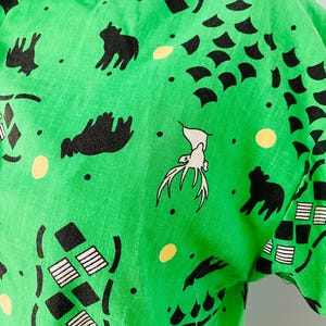 Puede incluir: Camisa verde brillante de manga corta con un patr&oacute;n repetido de siluetas de animales negros, formas geom&eacute;tricas y puntos amarillos. El dise&ntilde;o incluye ciervos, osos y formas abstractas. La tela parece ser ligera.