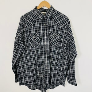 May include: A black and white plaid long-sleeved button-up shirt with two chest pockets. The shirt is hanging on a wooden hanger.