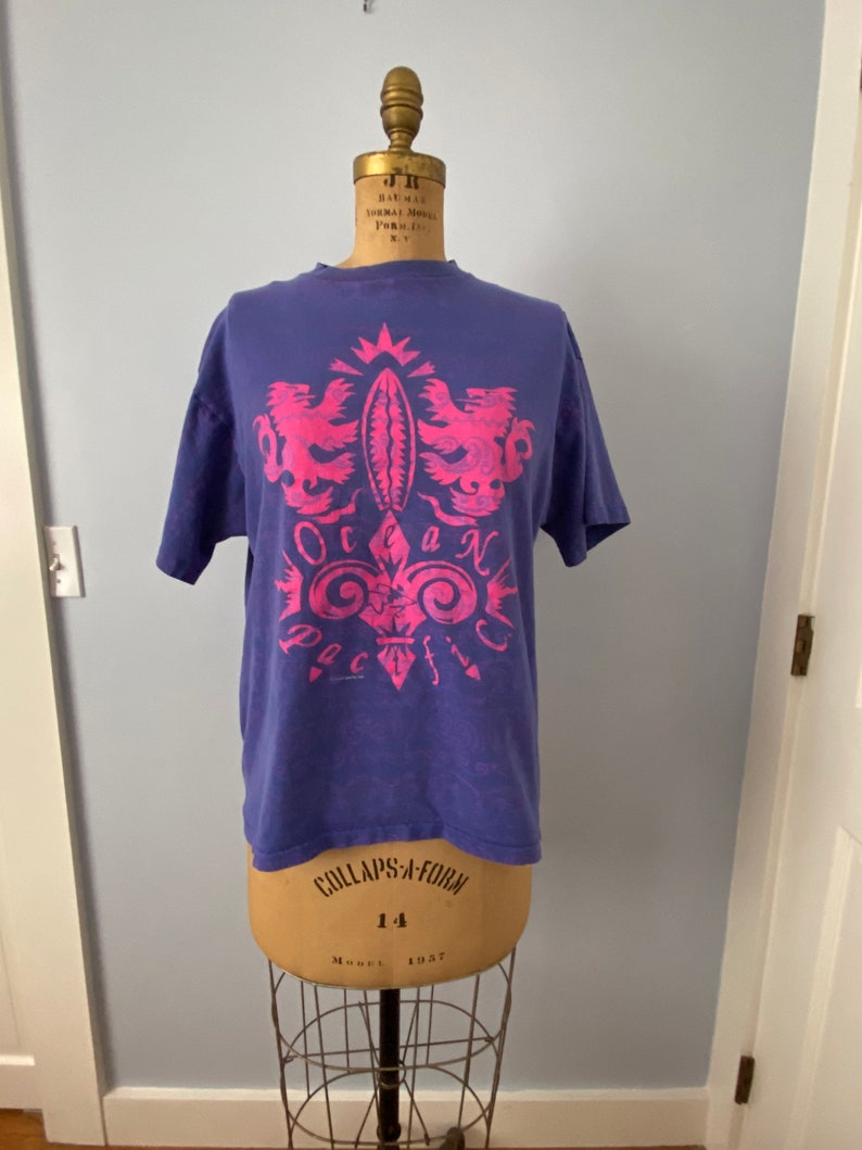 May include: A purple t-shirt with a pink graphic design of a crest with two birds and the text "Ocean Pacific".
