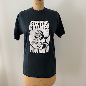 Puede incluir: Camiseta negra con un gráfico blanco de un hombre nativo americano con el texto "Stepping Stones Pow Wow" impreso en la parte delantera.