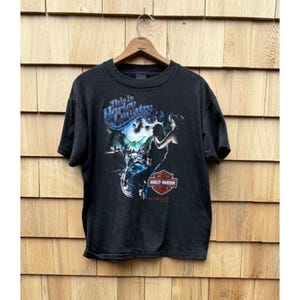 May include: Black Harley-Davidson t-shirt with a graphic featuring a motorcycle, a rider, and the text "This is Harley Country." The design includes blue, white, and red accents, and the Harley-Davidson logo.