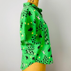 Puede incluir: Una camisa verde brillante con un estampado caprichoso de animales negros, formas geom&eacute;tricas y lunares amarillos. La camisa de manga corta se exhibe en un maniqu&iacute;.