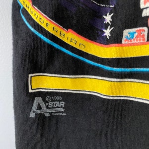 May include: Black t-shirt featuring a colourful graphic of a spaceship with the text "Thunderbird" and stars. The bottom of the shirt has a white and yellow stripe and the text "&copy;1993 A-STAR Canada, Inc."
