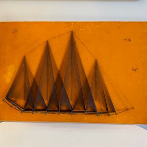 May include: A wall hanging with a geometric design of multiple triangles created with string on a mustard yellow background.
