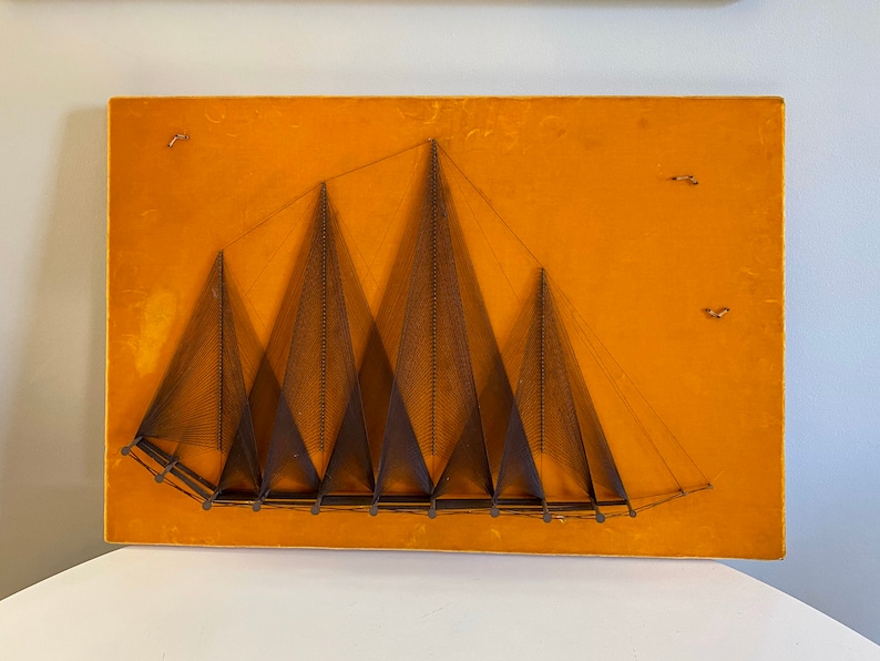 May include: A wall hanging with a geometric design of multiple triangles created with string on a mustard yellow background.