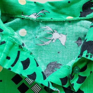 Puede incluir: Primer plano de una camisa verde con cuello con un patr&oacute;n repetido de ciervos blancos, osos negros, c&iacute;rculos amarillos y formas geom&eacute;tricas. La camisa tiene cierre de bot&oacute;n y est&aacute; hecha de tela ligera.