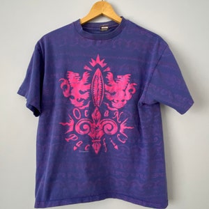 May include: A purple t-shirt with a pink graphic of a crest with two lions and the words "Ocean Pacific".