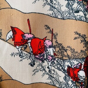 May include: Close-up of a fabric with a repeating pattern of a landscape scene. The design features figures on horseback, rendered in red, pink, and white, set against a backdrop of beige and brown hills and stylized trees.