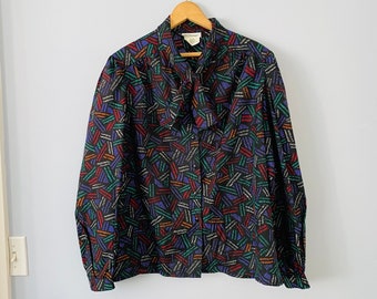 May include: A black long-sleeved blouse with a colorful geometric pattern. The blouse has a bow tie at the neck and a button-up front.