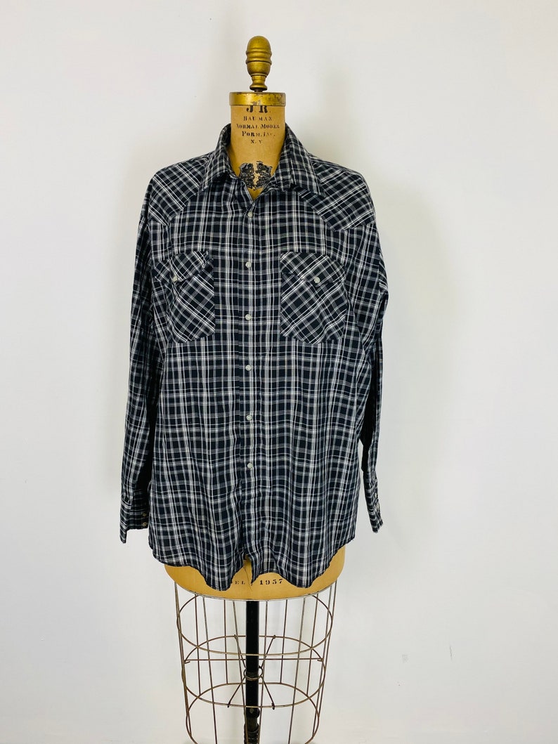 May include: A black and white plaid long-sleeved shirt with a button-down collar and two chest pockets.