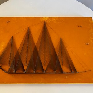 May include: A wall hanging made of string art depicting a series of brown triangles on a yellow background.