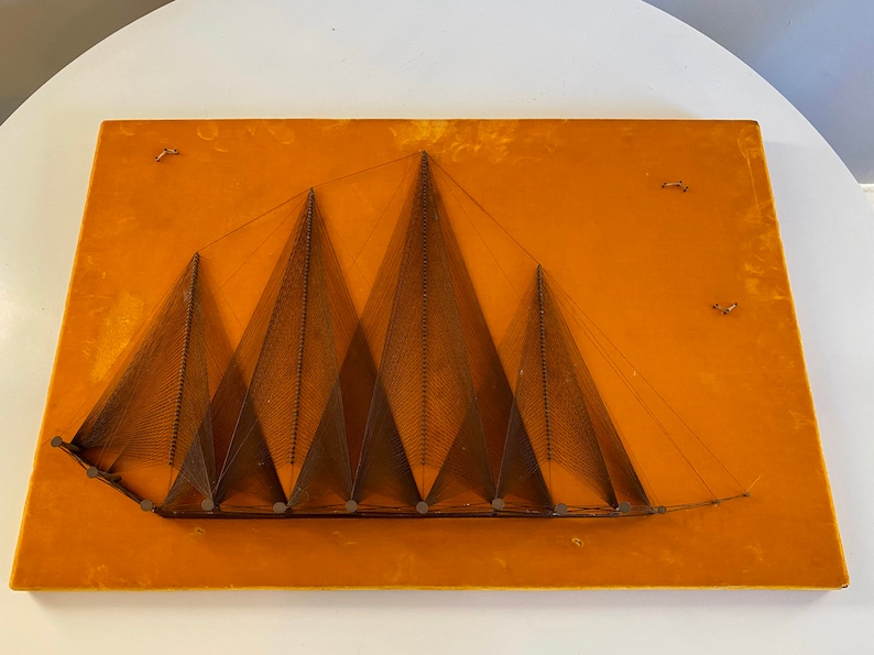 May include: A wall hanging made of string art depicting a series of brown triangles on a yellow background.