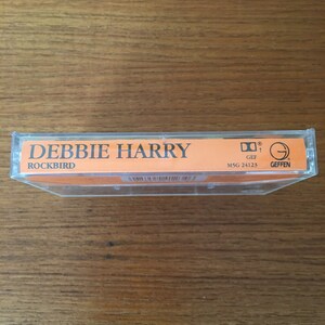 May include: A cassette tape with a orange label. The label says "Debbie Harry" and "Rockbird". The cassette tape is in a clear plastic case. The case has a sticker with the Geffen Records logo and the number "MSG 24123".