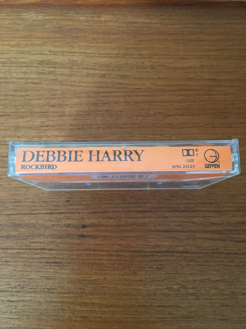 May include: A cassette tape with a orange label. The label says "Debbie Harry" and "Rockbird". The cassette tape is in a clear plastic case. The case has a sticker with the Geffen Records logo and the number "MSG 24123".