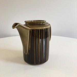 Puede incluir: Una tetera de cer&aacute;mica con rayas marrones y negras, con un pico y un asa.