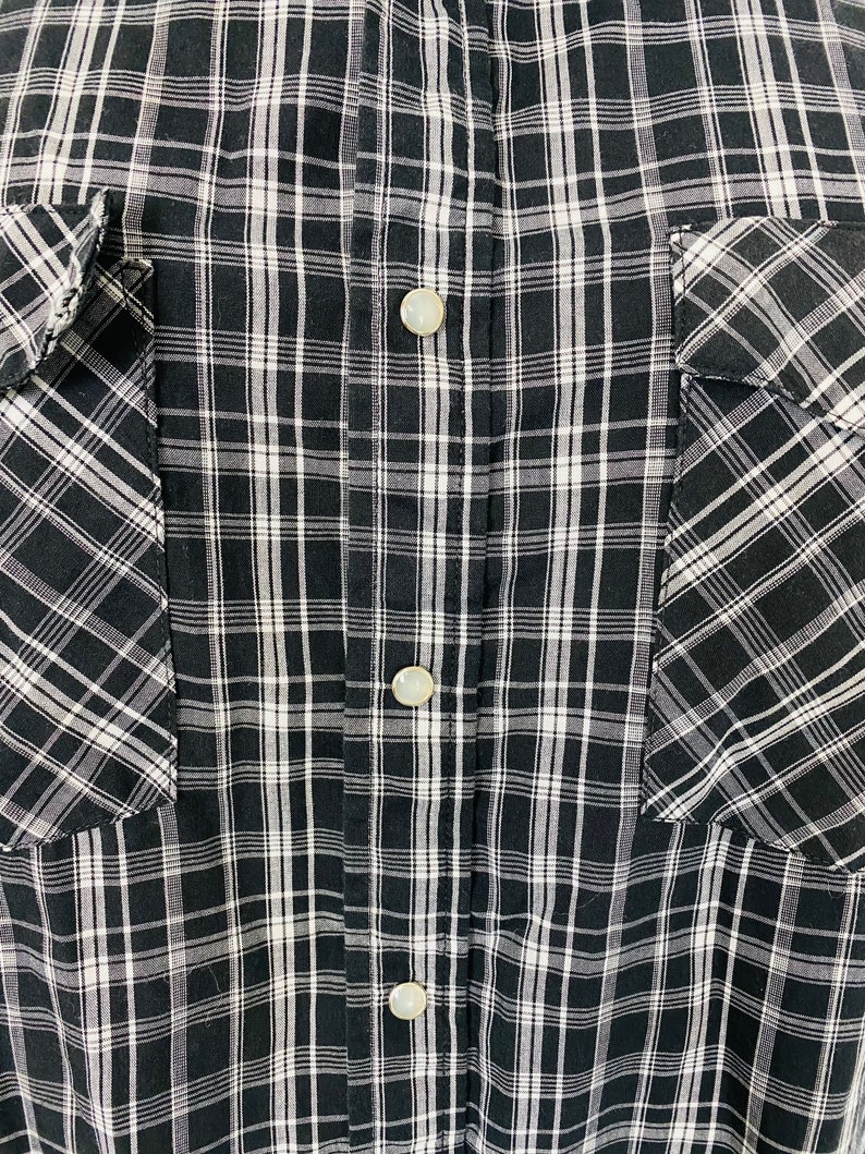 May include: Black and white plaid button-up shirt with two chest pockets.