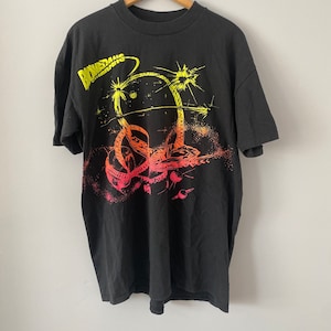 Op de afbeelding: Zwart T-shirt met een kleurrijke grafische print van een slang in de ruimte. De grafiek toont een slang die om een planeet is gewikkeld met sterren en andere hemellichamen op de achtergrond. De tekst "Biohazard" is in geel op het shirt gedrukt.