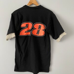 May include: Black t-shirt with a white underlay and a large orange number "28" printed on the back.
