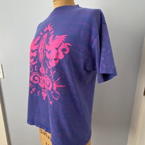 May include: A purple t-shirt with a pink graphic of a stylized design with the word "Ocean" in the center.